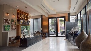 Un hall d’hôtel moderne doté d’un comptoir d’accueil, d’un espace salon et de grandes fenêtres donnant sur la rue.