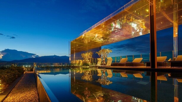 Un bâtiment moderne doté d’une façade en verre, d’une piscine et de chaises longues.