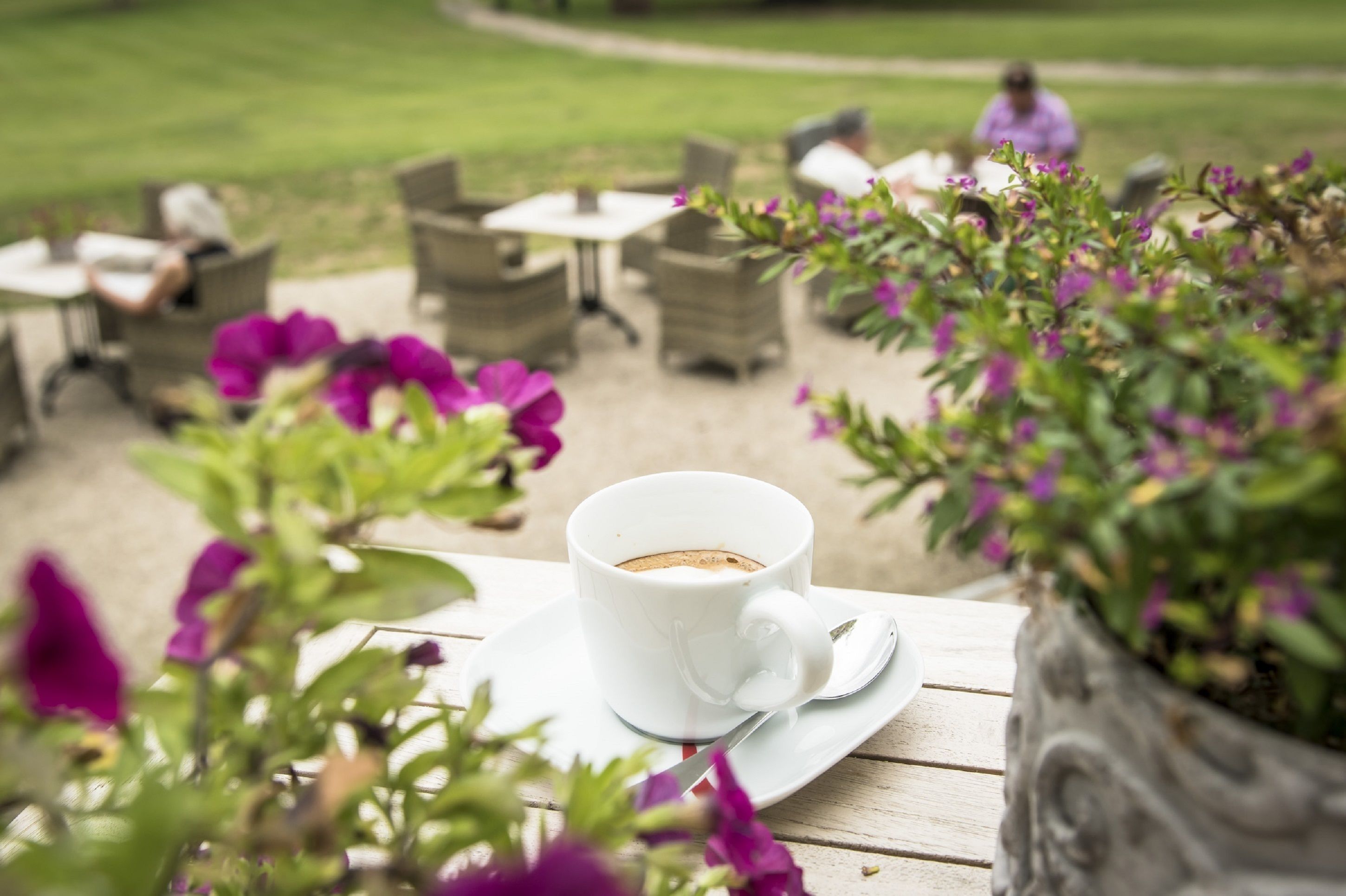 A white cup of coffee on a white saucer on a wooden table.