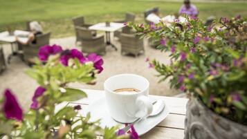 A white cup of coffee on a white saucer on a wooden table.