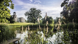 Een rustgevende omgeving aan een meer, met een historisch gebouw, weelderige begroeiing en een houten steiger.