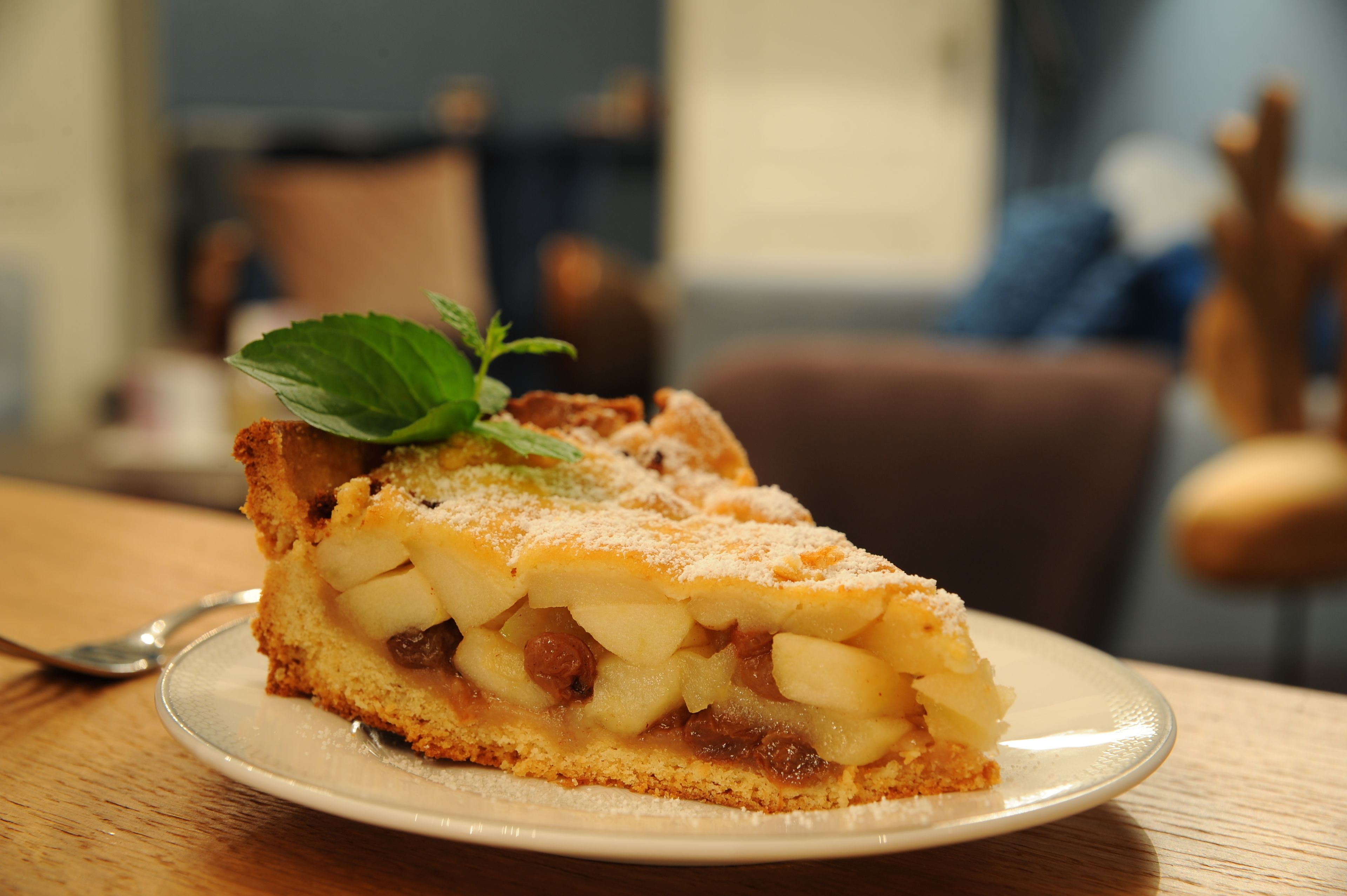 Una porción de tarta de manzana en un plato, adornada con una hoja de menta, sobre una mesa de madera.