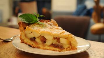 Una porción de tarta de manzana en un plato, adornada con una hoja de menta, sobre una mesa de madera.
