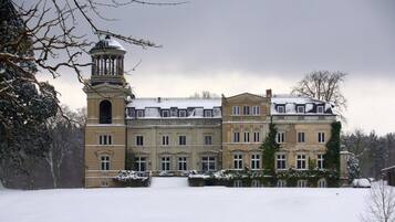 A large, historic building with a prominent tower and multiple windows, surrounded by snow.
