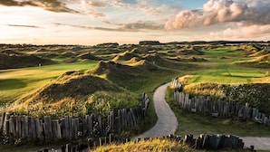 Een golfbaan met een slingerende pad, houten omheiningen en glooiende heuvels.