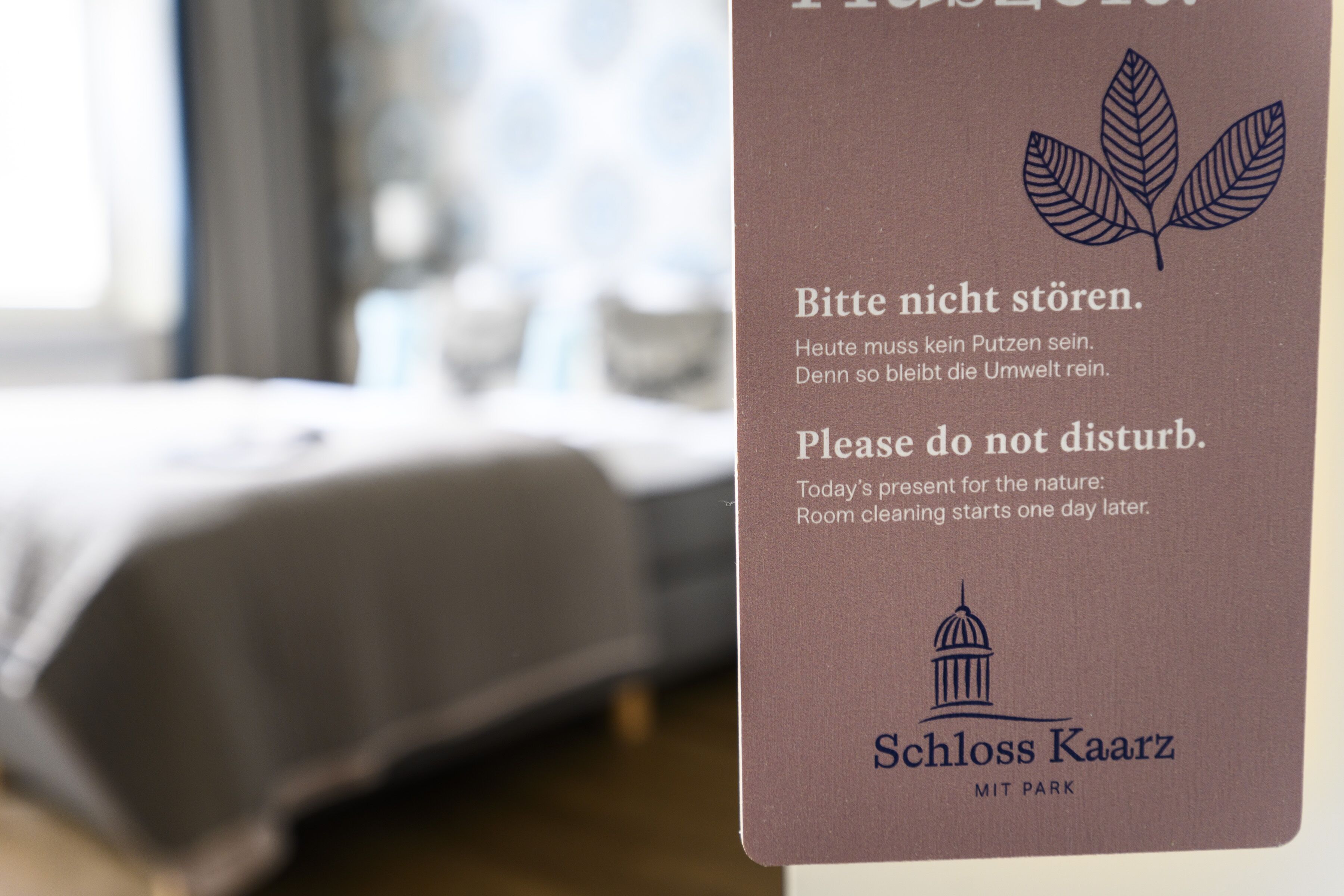 A sign in a hotel room with text in German and English advising guests not to disturb as room cleaning starts the next day. The sign features a leaf and a building icon.