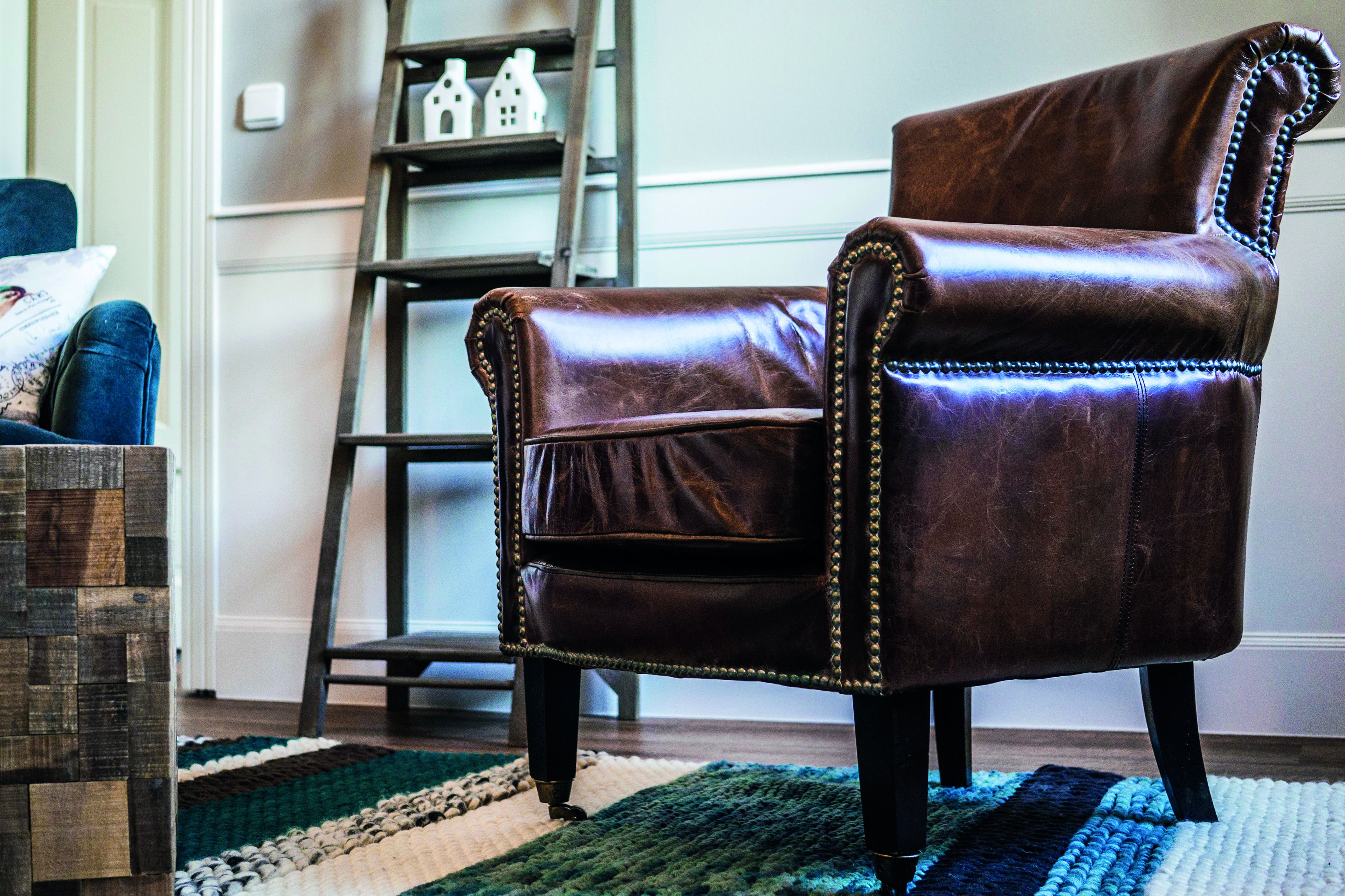 A brown leather armchair with a high back and decorative studs, positioned in a room with a wooden floor and a green and white striped rug.