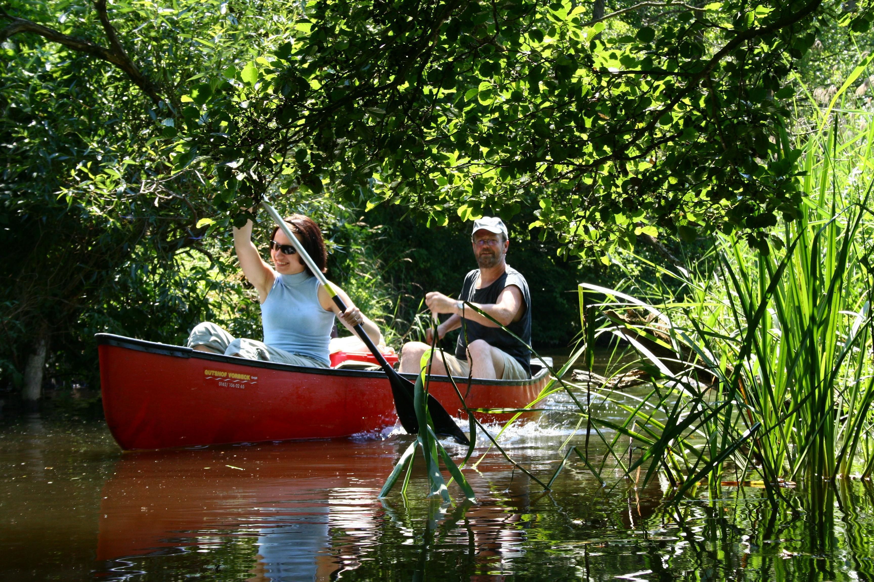 Two people in a red boat on a calm river surrounded by lush greenery.