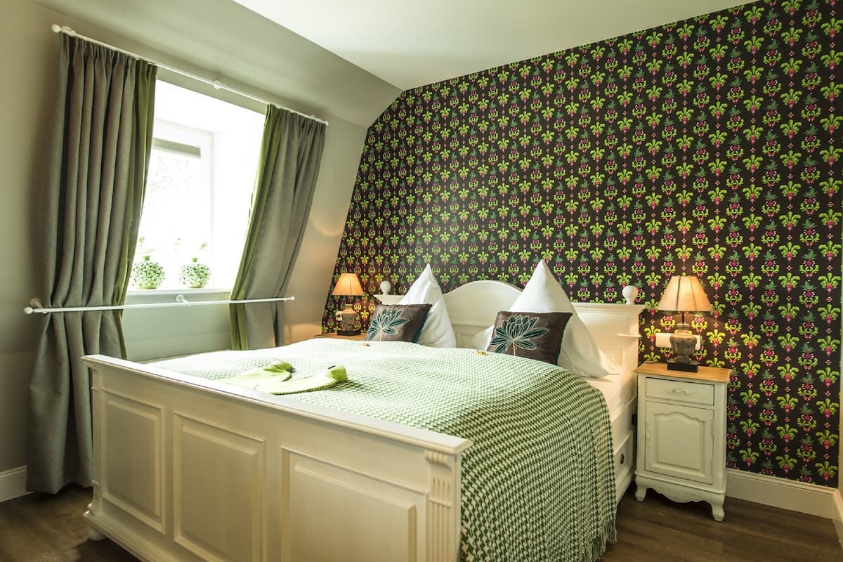 Ein Schlafzimmer mit einem Bett, zwei Nachttischen, einem Fenster mit Vorhängen und raumschicker Tapete.