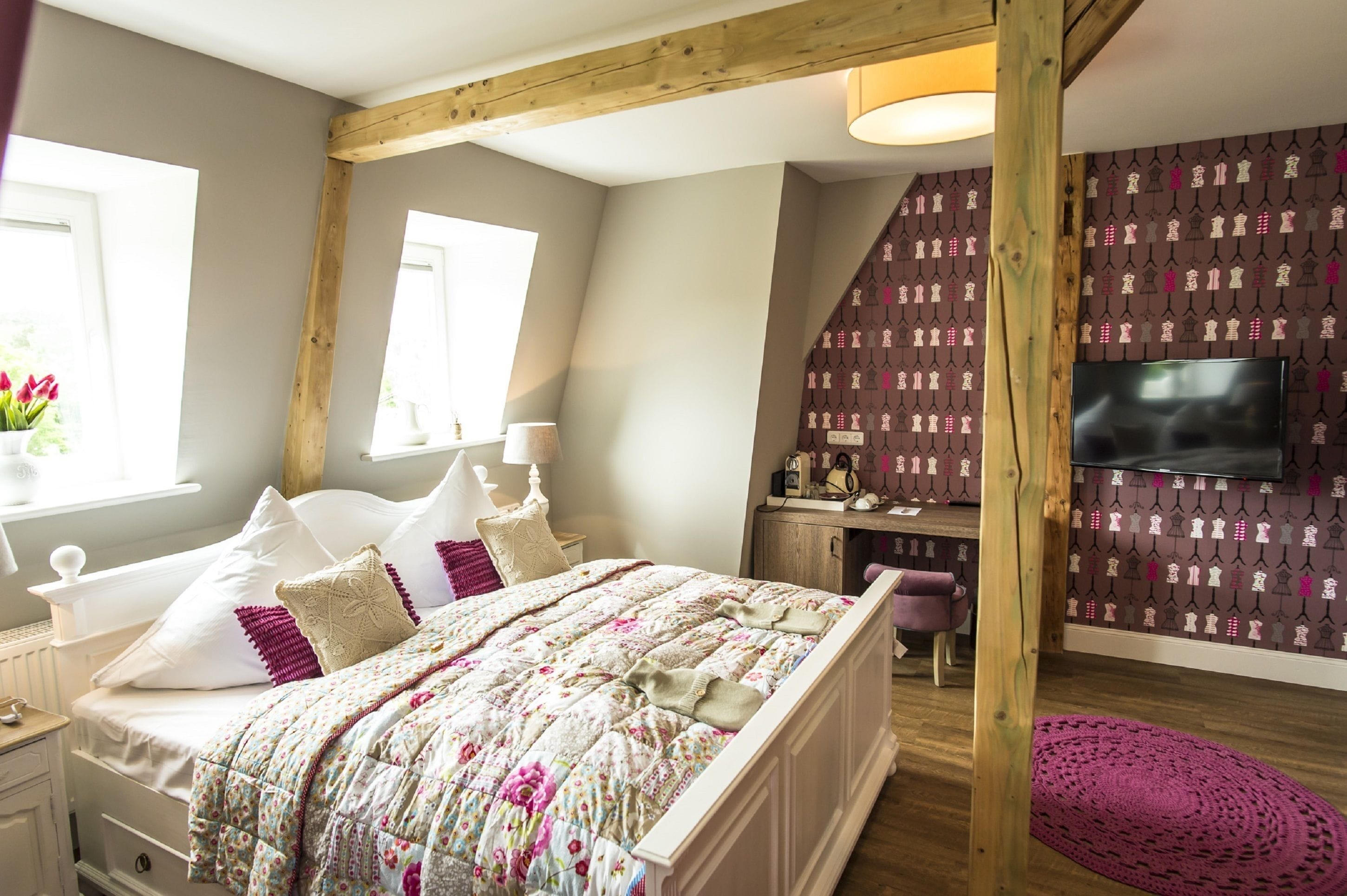 Ein Schlafzimmer mit einem Bett, Nachttischen, einem Schreibtisch, einem Sessel, einem Fernseher und einer Wand mit Muster.