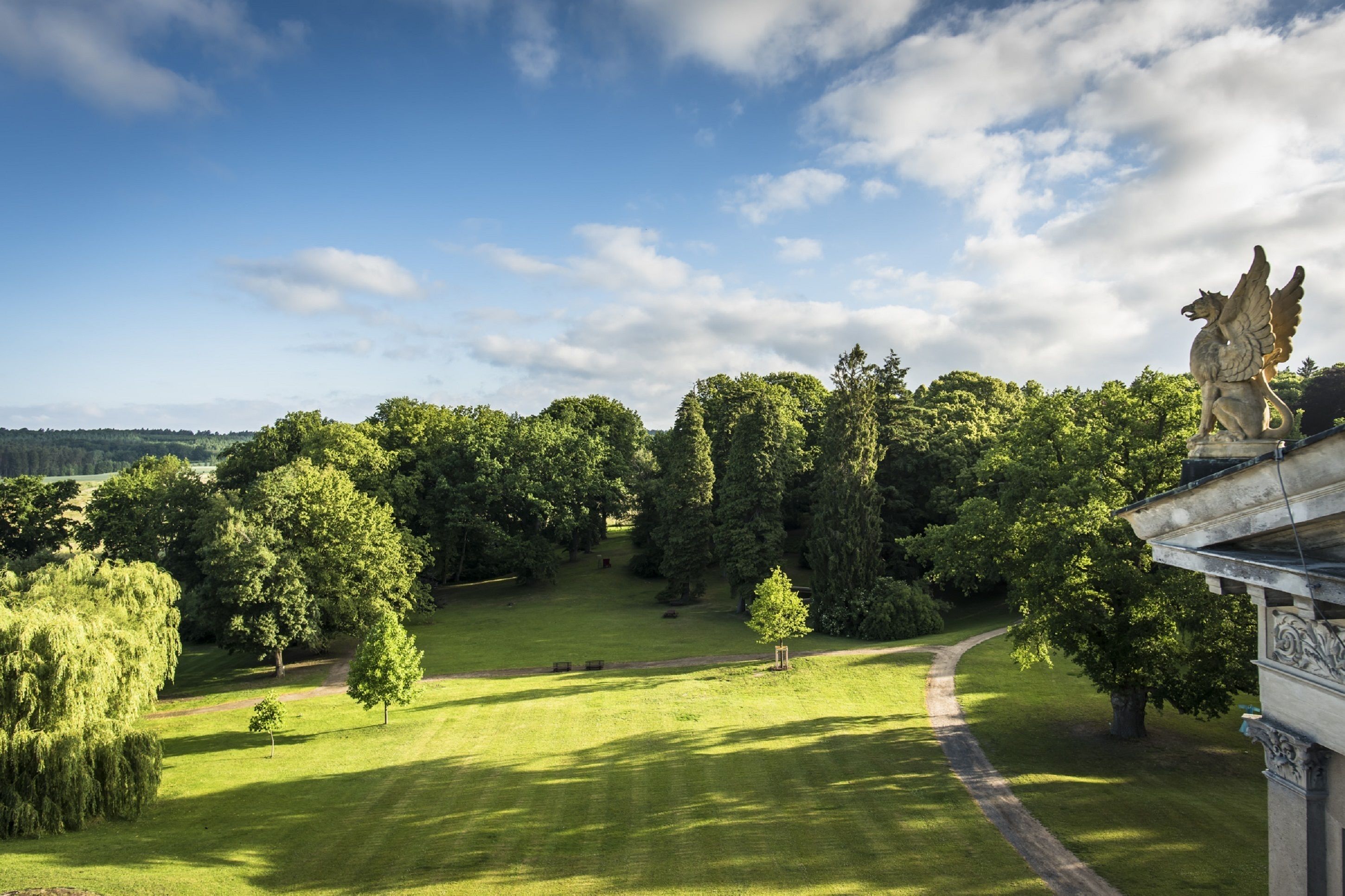 Ein angelegter Garten mit einer Statue, blauem Himmel und einem Weg.