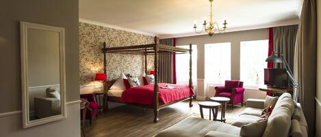 Une chambre spacieuse avec un lit à baldaquin, un coin salon avec un canapé et des fauteuils, une télévision et un lustre.
