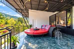 A modern outdoor seating area with a circular red bench, a potted plant, and a view of lush greenery. - Luxury villa mountain view 10BR /Private chef available (Soi Themrat Chalong Muang)