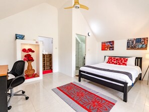 A bedroom with a bed, a desk, a chair, a vase with flowers, and a door leading to a bathroom. - Luxury villa mountain view 10BR /Private chef available (Soi Themrat Chalong Muang)