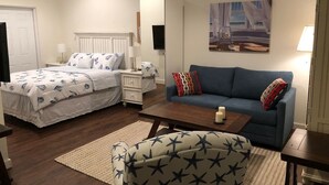 A bedroom with a bed, a blue sofa, a chair, a bedside table, a lamp, and a painting on the wall.