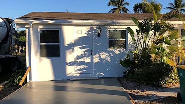 A single-story house with a concrete driveway, a white exterior, and a small porch area.