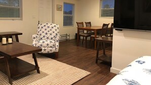 A compact living space with a dining area, a TV mounted on the wall, and a patterned armchair.