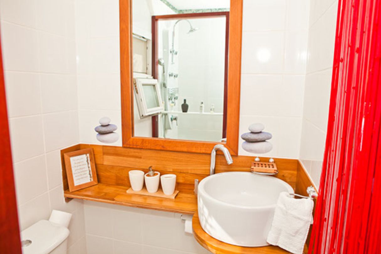 Une salle de bain avec un lavabo blanc, un meuble-lavabo en bois, un miroir et un rideau rouge.
