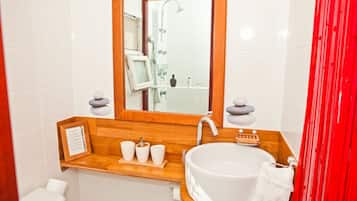 Un baño con lavamanos blanco, tocador de madera, espejo y cortina roja.