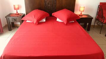 A bed with a red bedspread and two pillows, flanked by two nightstands with lamps, in a room with a wooden headboard and a chair with a red cushion.