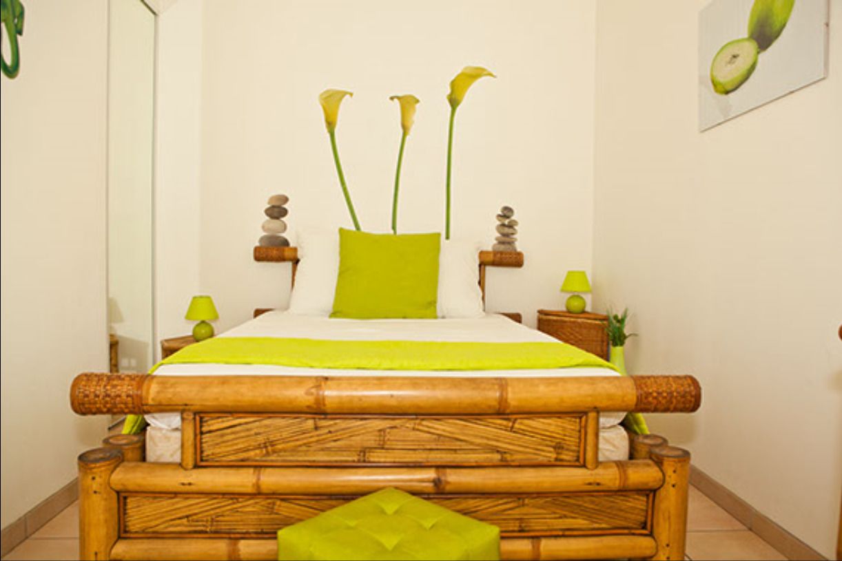 A bed with a bamboo headboard, a green pillow, and a green throw blanket. There are two bedside tables with lamps and decorative items.