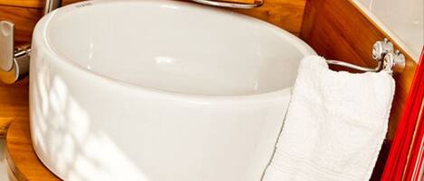 A large, oval-shaped white sink with a wooden countertop, a white towel, and a soap dish.