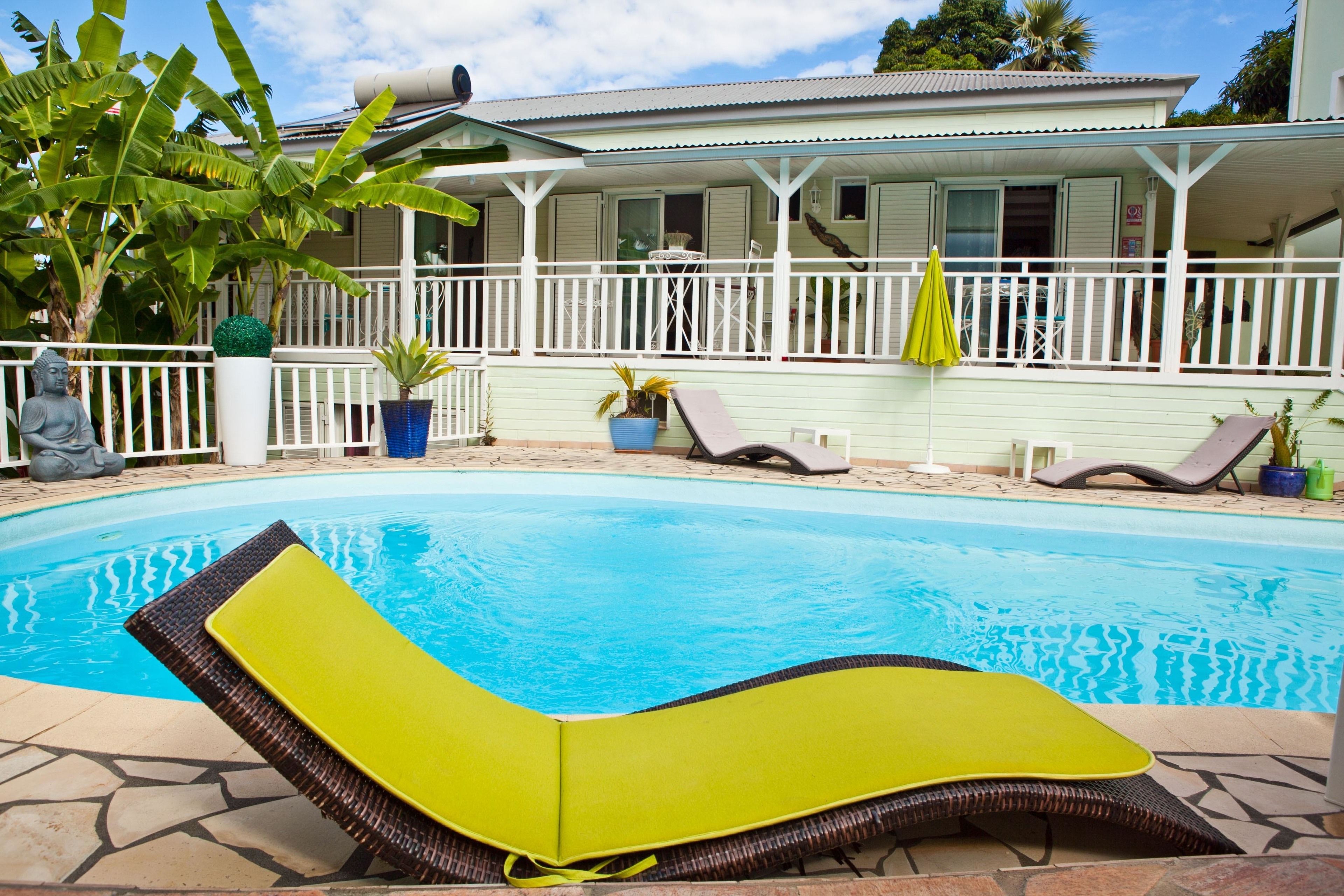 A swimming pool with lounge chairs, a covered patio, and a house in the background.