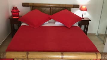 Un lit avec une couvre-lit rouge, deux oreillers rouges et une tête de lit en bois. Il y a deux tables de chevet avec des lampes.