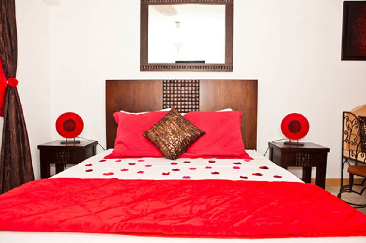 Una cama con colcha y almohadas rojas, un cabecero de madera y dos mesitas de noche con adornos rojos.