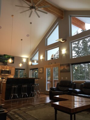 A spacious living area with a high ceiling, large windows, a kitchen with a microwave, and a seating area with a coffee table. - 2 bedroom house with hot tub located in Seward (Seward)