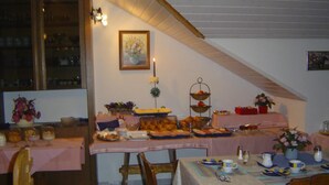 A dining area with a high ceiling and exposed beams, featuring a long table set with various dishes and a small altar with candles. - Landhotel Mühlberg (Moessingen)