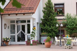 A building with a tiled roof, a glass door entrance, and a small patio area with outdoor seating and potted plants. - Landhotel Mühlberg (Moessingen)