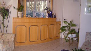 A reception area with a wooden counter, a large window with curtains, and several potted plants. - Landhotel Mühlberg (Moessingen)