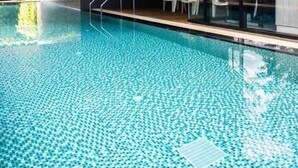 Ein moderner, überdachter Swimmingpool mit klarem Wasser, einer Metallleiter und weißen Liegestühlen.