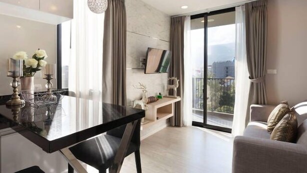 Ein modernes Wohnzimmer mit einem Glastisch, einer Couch und einem Balkon mit Vorhängen.
