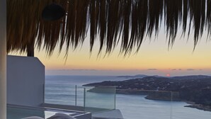 A modern room with a glass balcony overlooking a coastal view at sunset. - Myconian Panoptis Escape - Small Luxury Hotels of the World (Mykonos)