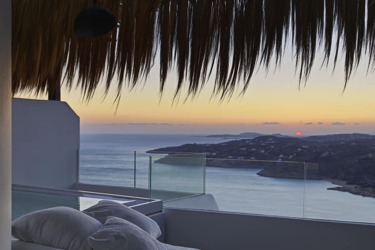 A modern room with a glass balcony overlooking a coastal view at sunset.