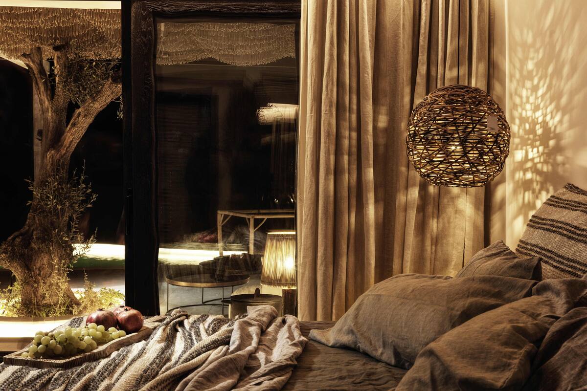 A cozy bedroom with a bed, a woven lamp, and a view of a dining area.
