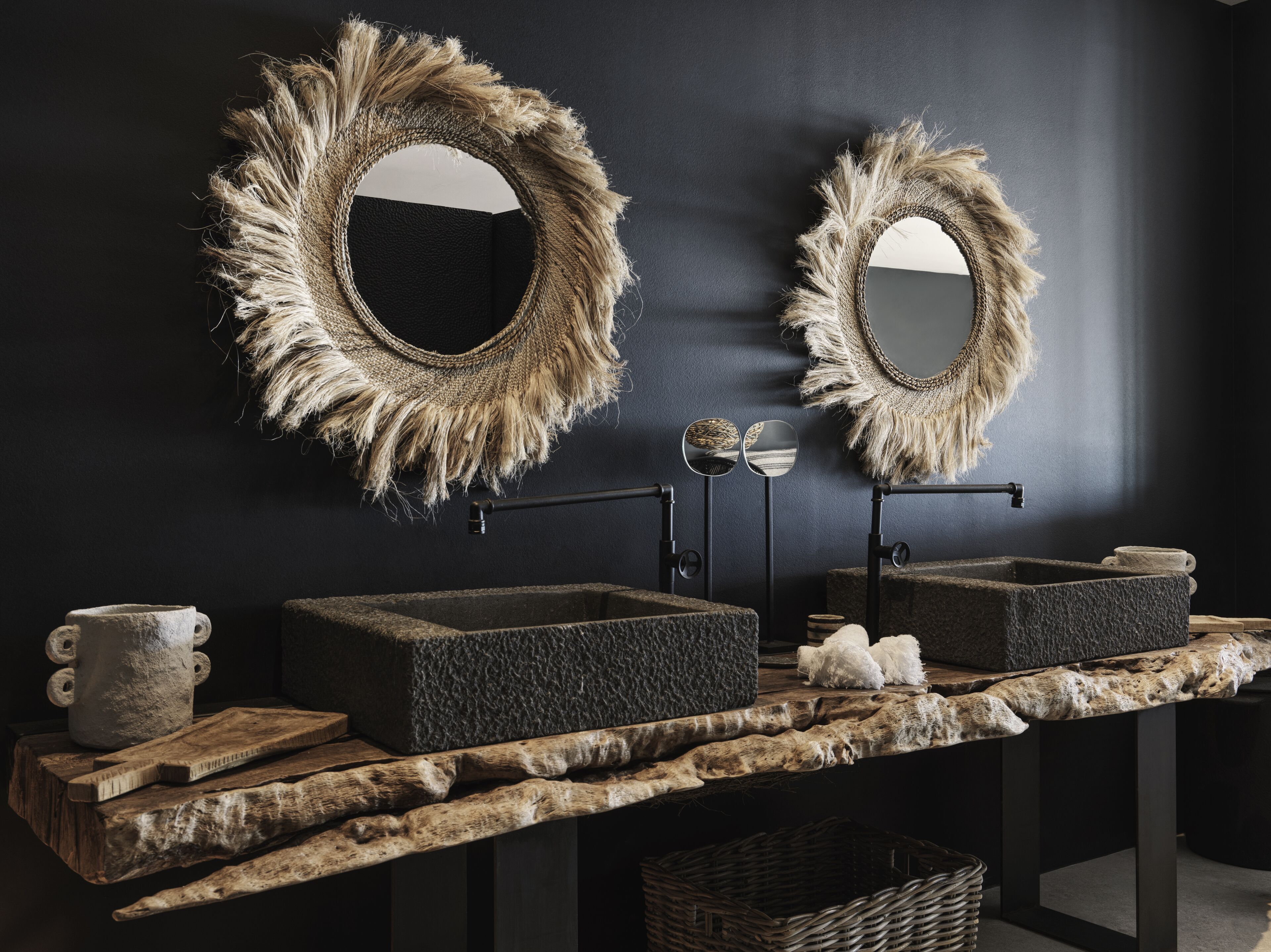 A bathroom with two large mirrors with frayed edges, a stone sink, and a wooden vanity.