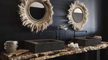 A bathroom with two large mirrors with frayed edges, a stone sink, and a wooden vanity.
