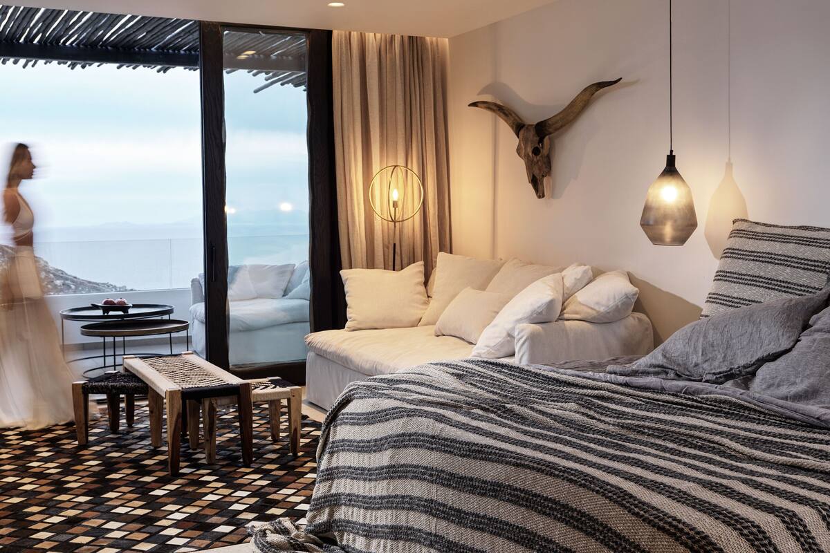 A modern hotel room with a large bed, a sofa, a small table, and a view of the ocean.