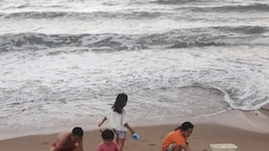 Escena de playa con niños jugando en la arena, un refrigerador y un recipiente para agua.