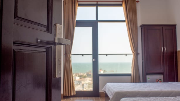 Un dormitorio con dos camas, un ventanal con cortinas y vista al mar, además de un armario de madera.