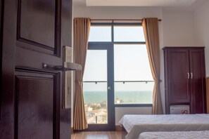 A bedroom with two beds, a large window with curtains, a view of the sea, and a wooden wardrobe. - Moon Hotel (Phu Thuy)