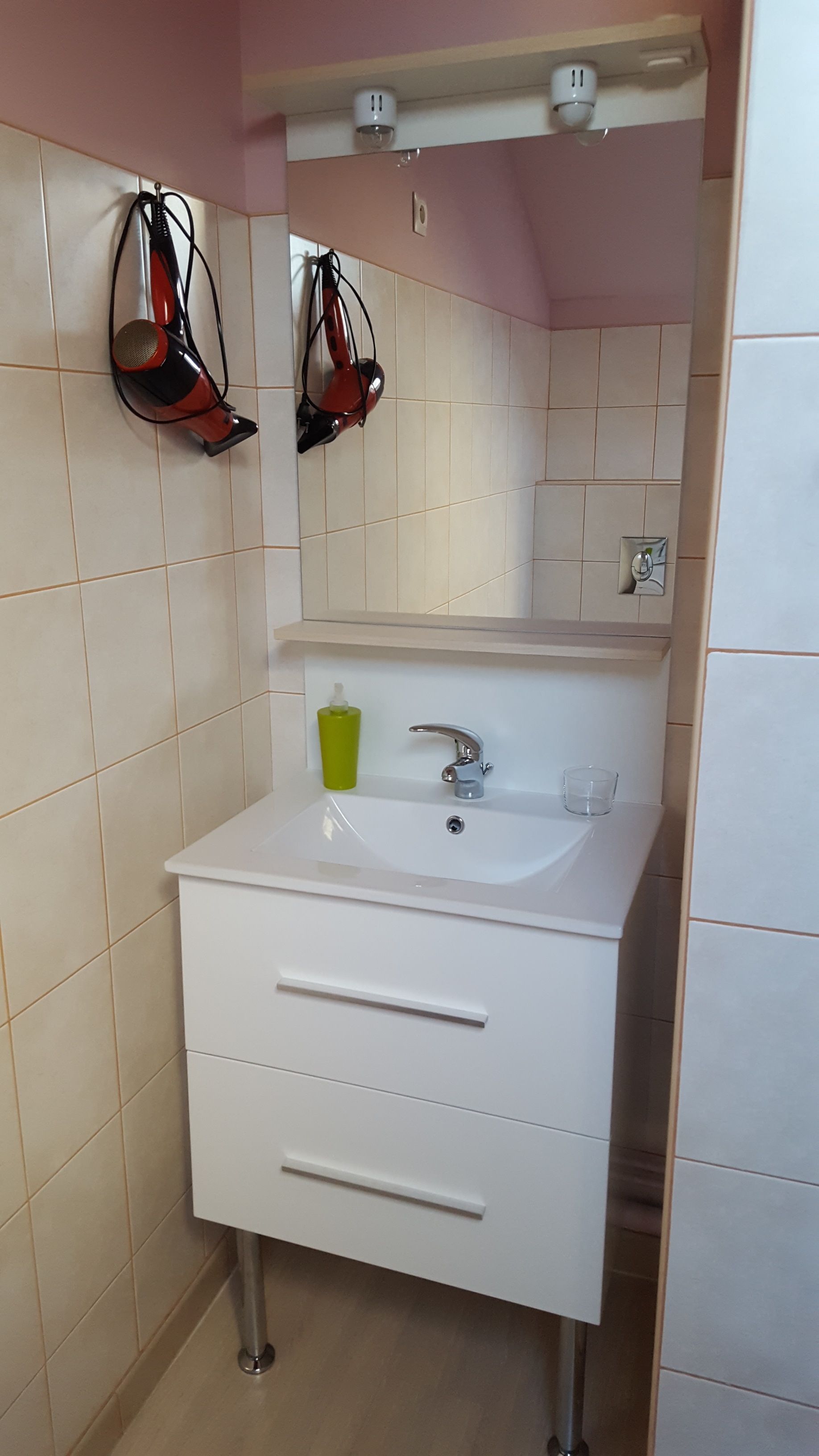 Ein Badezimmer mit einem weißen Waschbecken, einem Spiegel und einem roten Föhn an der Wand.