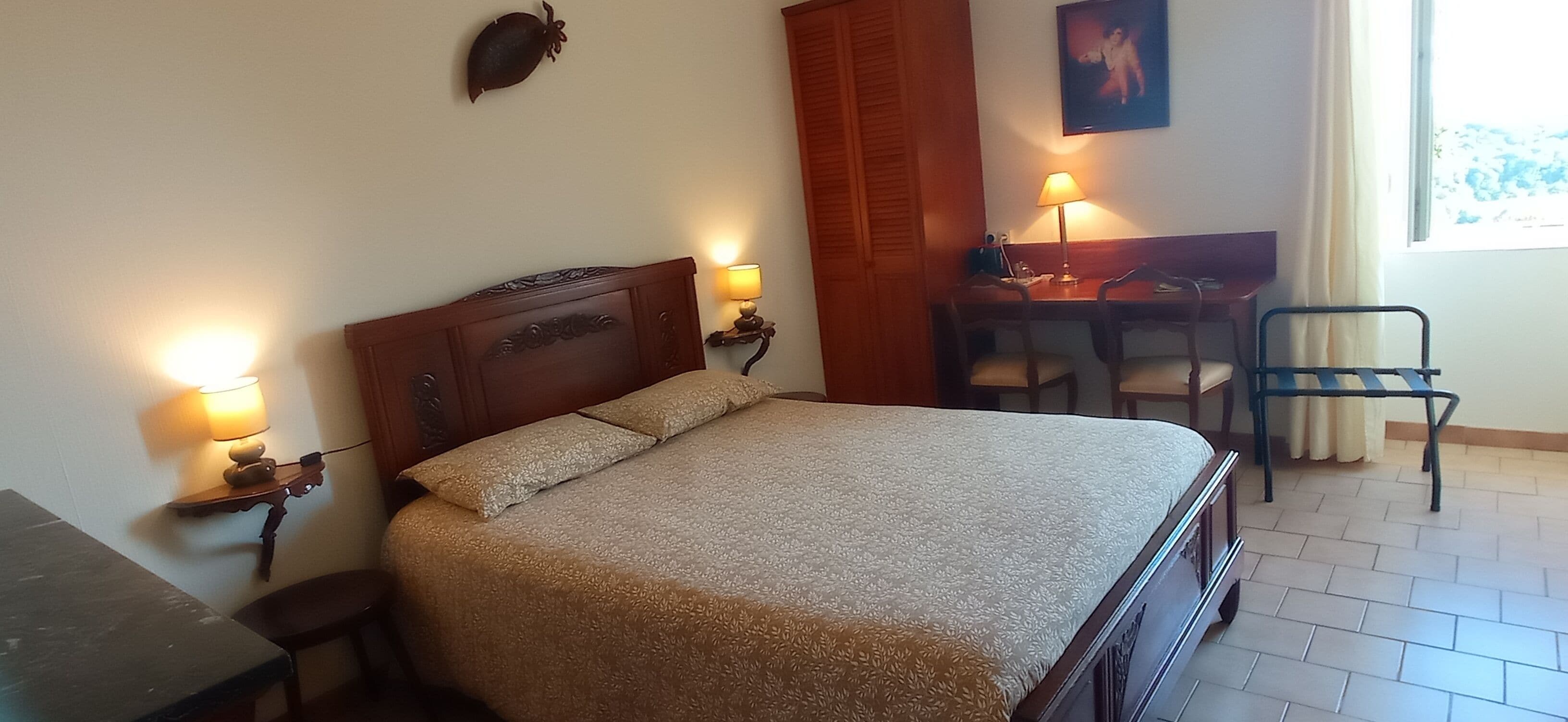 A bedroom with a bed, bedside lamps, a desk, and a chair.