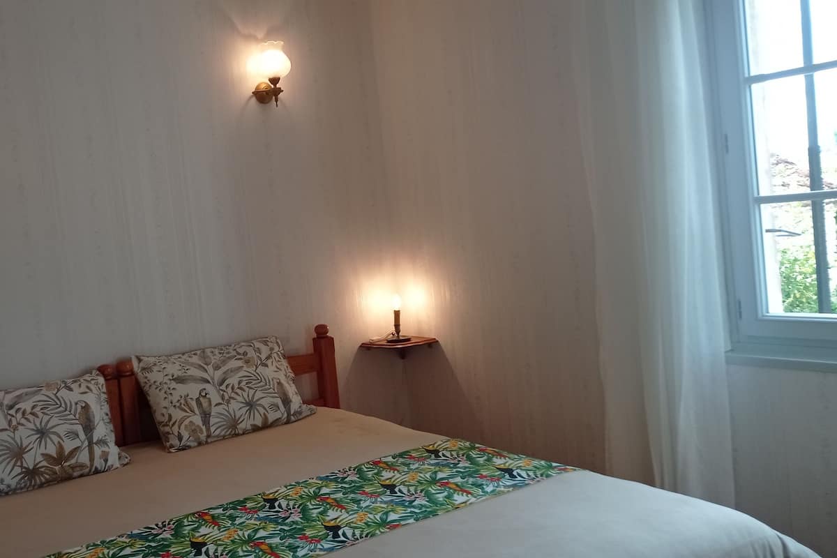 A bedroom with a bed, two wall-mounted lamps, a window, and a nightstand with a candle.