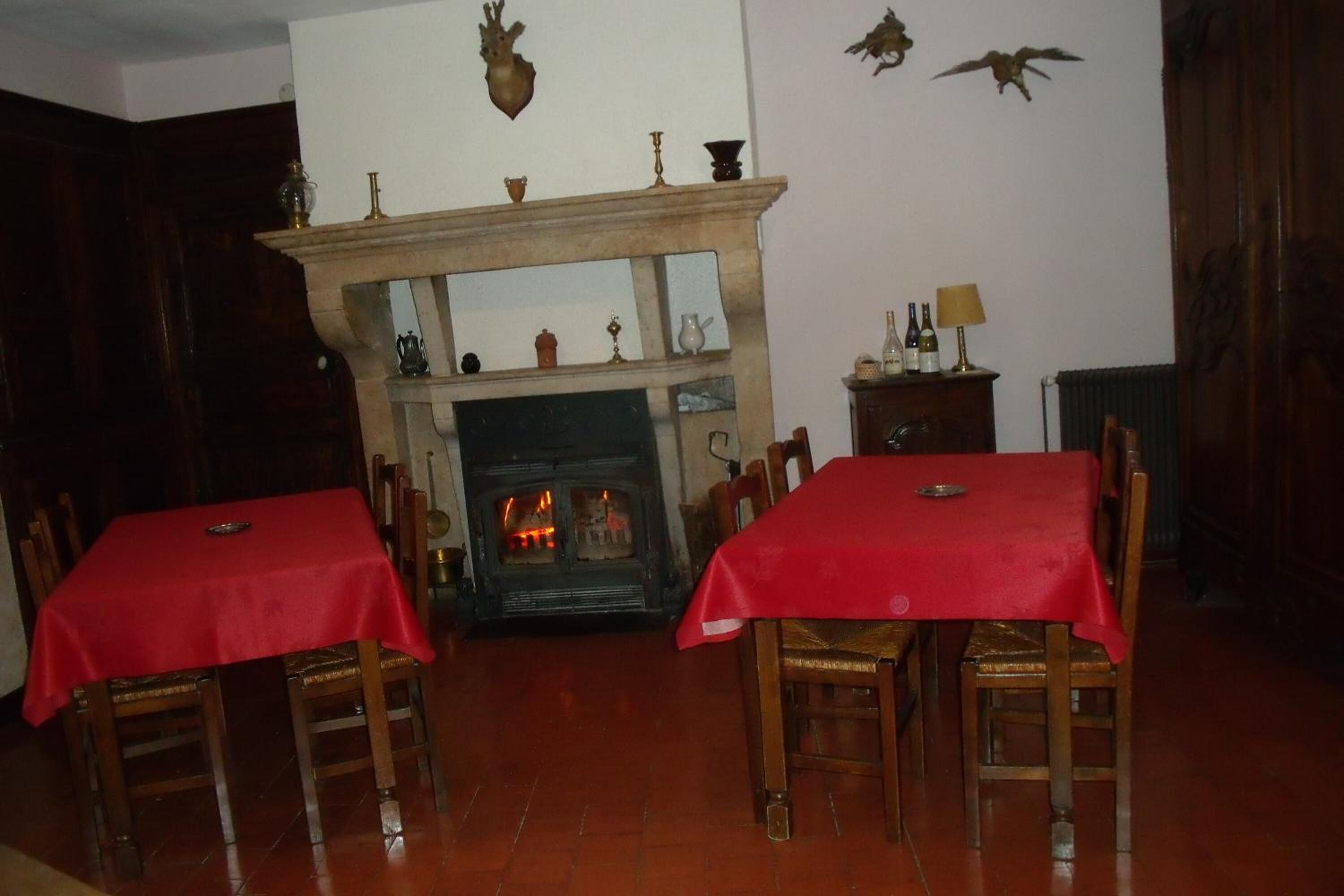 A dining room with two tables covered in red tablecloths, wooden chairs, a fireplace, and wall-mounted decorations.