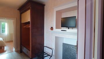 A room with a wooden wardrobe, a television on a mantelpiece, and a chair near a fireplace.