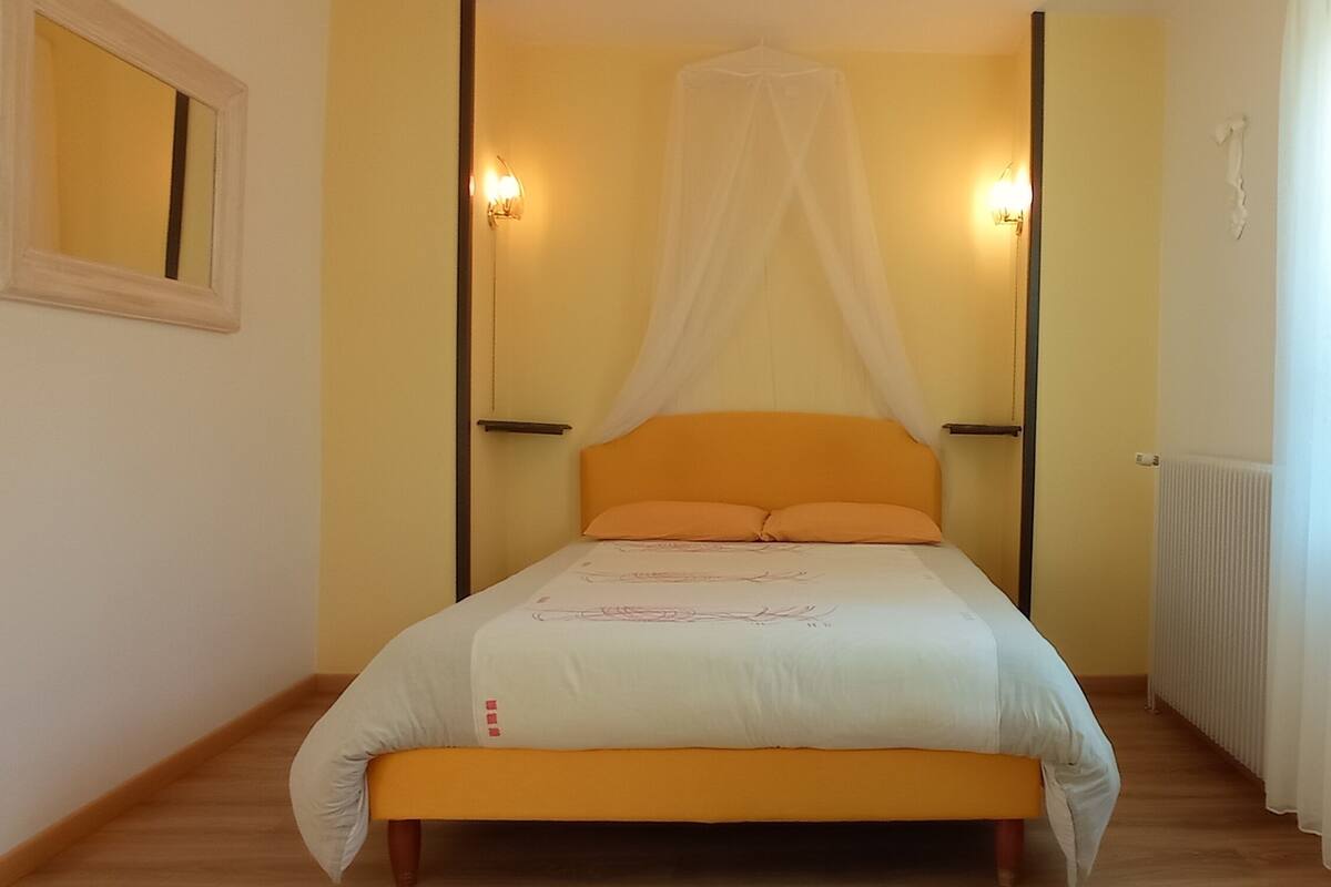 A bedroom with a bed, a bedside table, a nightstand, a window with curtains, and a door.